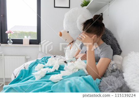 A young teenager lies in her bed because she is sick and has a chronic headache. A young teenager lies in her bed because she is sick and has a chronic headache. 115139224