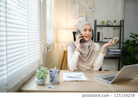 A woman wearing a hijab is talking on her cell phone in a cubicle 115139239