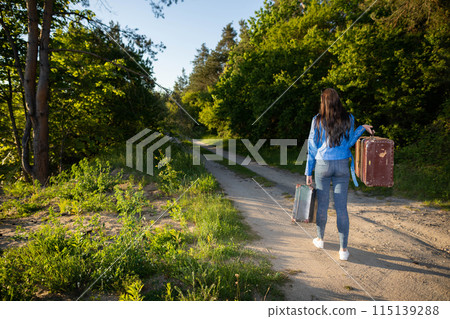 Return home to the countryside after a successful holiday. Walk along the country sandy road with old heavy suitcases among green trees. Return home to the countryside after a successful holiday. Walk along the country sandy road with old heavy suitcases among green trees. 115139288