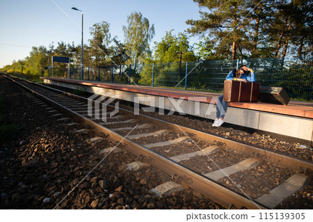 A teenager is sitting in a forbidden place on a railway platform and her legs are hanging over the railway tracks. Waiting for a late train. 115139305