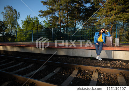 A teenager is sitting in a forbidden place on a railway platform and her legs are hanging over the railway tracks. Waiting for a late train. 115139307
