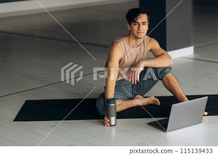 Young fit man watch sport tutorial during break. Handsome man drink water from steel bottle and use laptop Young fit man watch sport tutorial during break. Handsome man drink water from steel bottle and use laptop 115139433