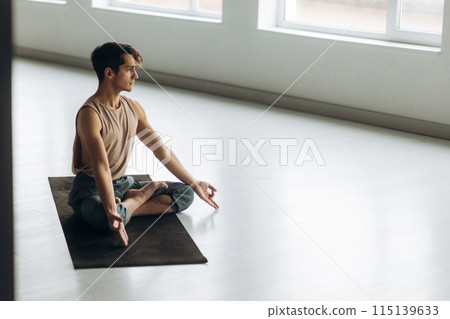 Side view of handsome calm focused guy sitting on floor meditating relaxation. Yoga man concept Side view of handsome calm focused guy sitting on floor meditating relaxation. Yoga man concept 115139633