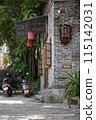The entrance of a cozy brick building adorned with parked mopeds and surrounded by greenery 115142031
