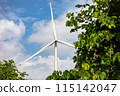 Wind turbine blades against blue sky and green foliage, promoting clean energy use 115142047