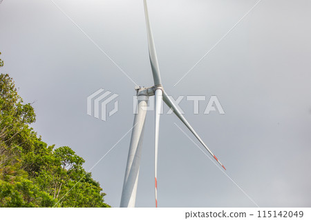 Wind Turbine Generating Clean Renewable Energy Amid Lush Greenery and Overcast Sky Wind Turbine Generating Clean Renewable Energy Amid Lush Greenery and Overcast Sky 115142049