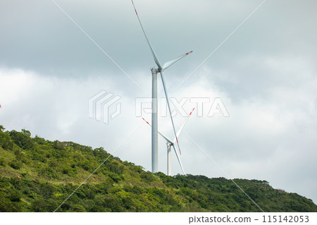 Wind turbines create a serene scene in a verdant landscape under an overcast sky Wind turbines create a serene scene in a verdant landscape under an overcast sky 115142053