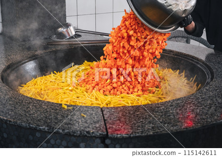 male chef adds carrots to a cauldron to cook traditional Uzbek pilaf in kitchen at a restaurant in Uzbekistan male chef adds carrots to a cauldron to cook traditional Uzbek pilaf in kitchen at a restaurant in Uzbekistan 115142611