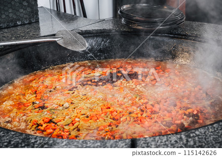 carrots, chickpeas and raisins are boiled in a cauldron to cook traditional Uzbek pilaf in the kitchen of a restaurant in Tashkent, Uzbekistan carrots, chickpeas and raisins are boiled in a cauldron to cook traditional Uzbek pilaf in the kitchen of a restaurant in Tashkent, Uzbekistan 115142626