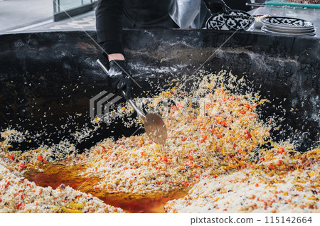 man cook puts cooked Uzbek pilaf from cauldron on plate. Traditional Oriental Arabic cuisine. Central Asian Pilaf Center Besh Qozon in Uzbekistan man cook puts cooked Uzbek pilaf from cauldron on plate. Traditional Oriental Arabic cuisine. Central Asian Pilaf Center Besh Qozon in Uzbekistan 115142664