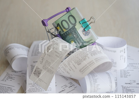 Euro bills bunch in shopping trolley surrounded by many paper receipts close up 115143857
