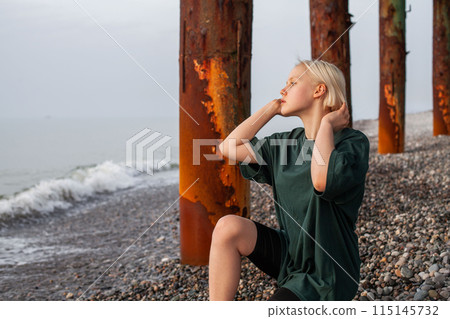 Posing young girl with short blonde bob hair and green t-shirt dress on cold sea beach Posing young girl with short blonde bob hair and green t-shirt dress on cold sea beach 115145732