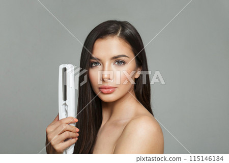 Stylish young healthy brunette woman holding hair iron and straightening her long smooth shiny hair Stylish young healthy brunette woman holding hair iron and straightening her long smooth shiny hair 115146184