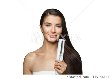 Isolated young healthy brunette woman holding hair iron and straightening her long smooth shiny hair 115146185