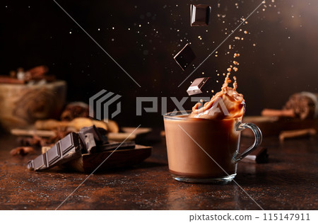 Pieces of dark chocolate fall into a glass of cocoa drink creating a beautiful splash. 115147911