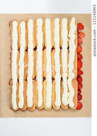 Rows of savoiardi cookies on sliced strawberries and covered with whipped cream. Rows of savoiardi cookies on sliced strawberries and covered with whipped cream. 115148903