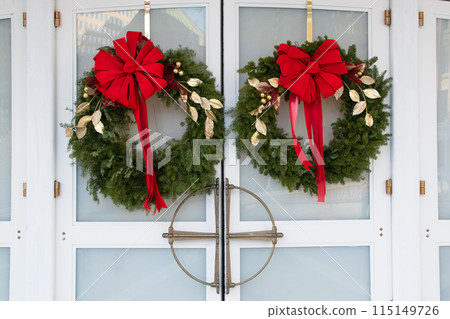 Christmas wreaths of fir branches with red velvet bows hang on a white door Christmas wreaths of fir branches with red velvet bows hang on a white door 115149726