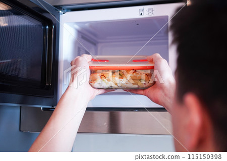 一名男子將耐熱玻璃特百惠放入微波爐加熱。 115150398