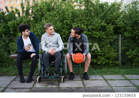 Young man in wheelchair spending free time outdoor with friends, having fun in city. Male friendship. Young man in wheelchair spending free time outdoor with friends, having fun in city. Male friendship. 115150658