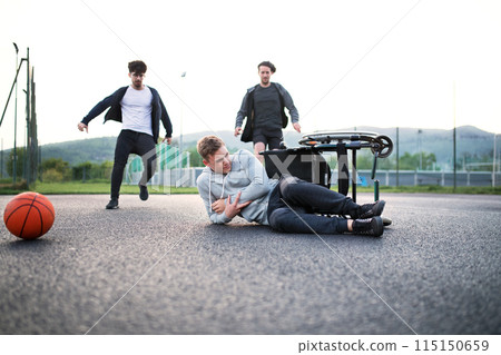 Young disabled man fall off wheelchair, fiends helping to sit back. Male friendship. Young disabled man fall off wheelchair, fiends helping to sit back. Male friendship. 115150659