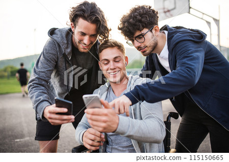 Young man in wheelchair spending free time outdoor with friends, taking selfie, having fun in city. Male friendship. Young man in wheelchair spending free time outdoor with friends, taking selfie, having fun in city. Male friendship. 115150665