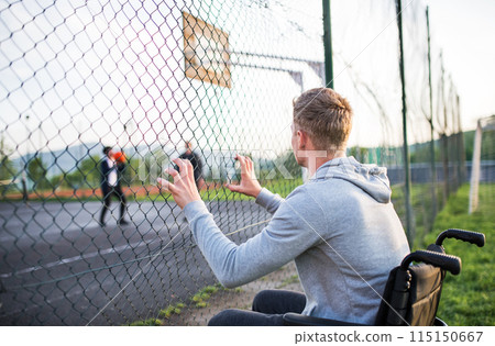 Disabled young man feeling excluded, want to play basketball with his friends, but because of wheelchair he can't. Disabled young man feeling excluded, want to play basketball with his friends, but because of wheelchair he can't. 115150667