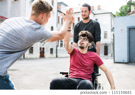 Young man in wheelchair spending free time outdoor with friends, having fun in city. Male friendship. 115150681