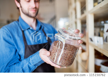 Handsome man working in package-free store using reusable containers. Zero waste shops offering package-free bulk goods and sustainable alternatives. Handsome man working in package-free store using reusable containers. Zero waste shops offering package-free bulk goods and sustainable alternatives. 115150762