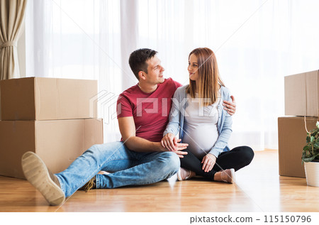 Beautiful young couple expecting a baby, moved into new home. Sitting among cardboard boxes. New beginnings. Beautiful young couple expecting a baby, moved into new home. Sitting among cardboard boxes. New beginnings. 115150796