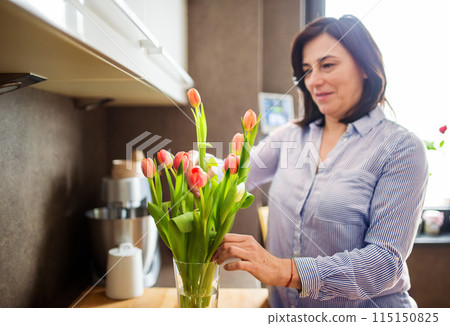 Portrait of beautiful mature woman with black hair and soft smile, holding bouquet of tulips. Portrait of beautiful mature woman with black hair and soft smile, holding bouquet of tulips. 115150825