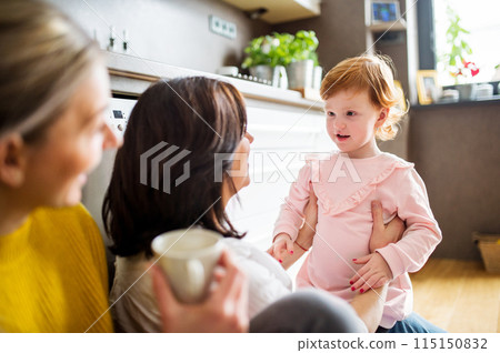 Mother, grandmother and little granddaughter in kitchen, sitting on floor. Family time, three generations of women in family. 115150832