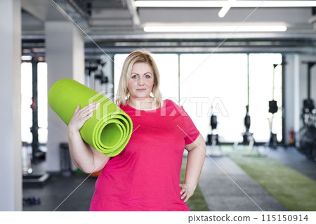 Portrait of overweight woman exercising in gym, holding gym mat. Portrait of overweight woman exercising in gym, holding gym mat. 115150914
