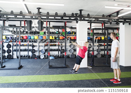 Overweight woman exercising in gym. Personal trainer couching her and helping her. 115150918