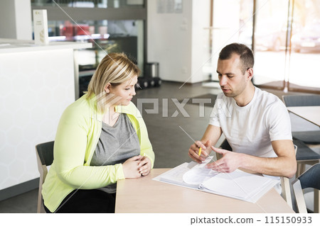 Overweight woman consulting with trainer, discussing fitness goals. Customizing exercise program with gym coach. Overweight woman consulting with trainer, discussing fitness goals. Customizing exercise program with gym coach. 115150933