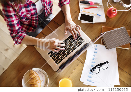 A beautiful university student is writing her thesis on a laptop, sitting at home on the couch. A beautiful university student is writing her thesis on a laptop, sitting at home on the couch. 115150935