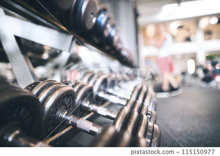 Rows of metal dumbbells on rack for strength training in gym. 115150977