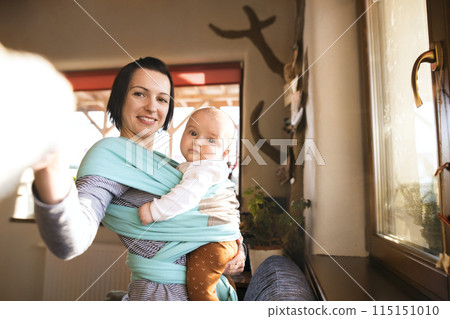 Mother holding small baby while dusting therir home, carrying him around in baby wrap. Household chores. Mother holding small baby while dusting therir home, carrying him around in baby wrap. Household chores. 115151010