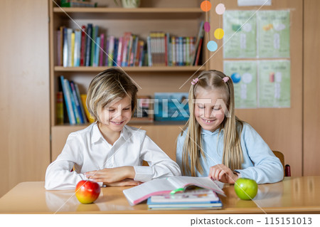 Portrait of two cute caucasian young blond little classmate friend kids eating apple in classroom at lunch time pause. Schoolchildren friendship. Healthy snack food. Back to school concept Portrait of two cute caucasian young blond little classmate friend kids eating apple in classroom at lunch time pause. Schoolchildren friendship. Healthy snack food. Back to school concept 115151013