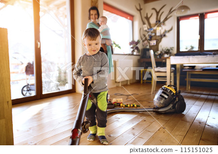 Young son helping mother with chores, vacuuming and cleaning their house. Weekly chores, weekend activities. 115151025