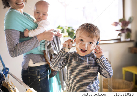 Young son helping mother with hosehold chores, hanging clothes on drying rack. Weekly chores, weekend activities. 115151026