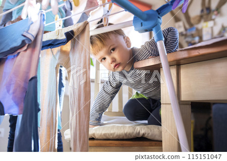 Young son helping mother with hosehold chores, hanging clothes on drying rack. Weekly chores, weekend activities. Young son helping mother with hosehold chores, hanging clothes on drying rack. Weekly chores, weekend activities. 115151047