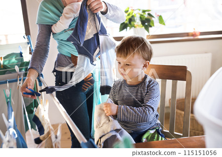 Young son helping mother with hosehold chores, hanging clothes on drying rack. Weekly chores, weekend activities. Young son helping mother with hosehold chores, hanging clothes on drying rack. Weekly chores, weekend activities. 115151056