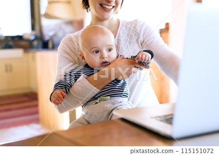 Mother with small baby working from homeoffice, typing on laptop. Mom paying bills online, holding small baby. 115151072