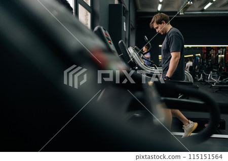 Side view of tired athletic man walking on treadmill preforming warming-up run routine exercise in gym. Sporty male walking on running track, working on health and fitness. Concept of healthy life. 115151564