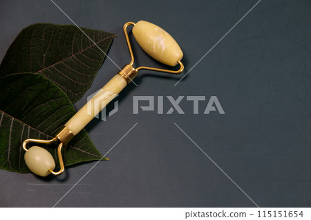 Jade face roller and gua sha scraper on grey background. Gua Sha face tool, green stone massage roller on a dark background with copy space, spa background with place for text, skin care 115151654