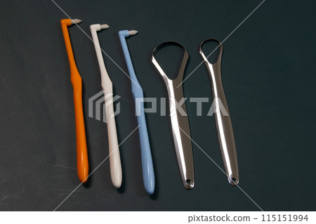 Tuft toothbrushes and tongue scraper on a dark background, tufted tapered trim toothbrush, single compact interdental interspace brush, tools for dental cleaning Tuft toothbrushes and tongue scraper on a dark background, tufted tapered trim toothbrush, single compact interdental interspace brush, tools for dental cleaning 115151994