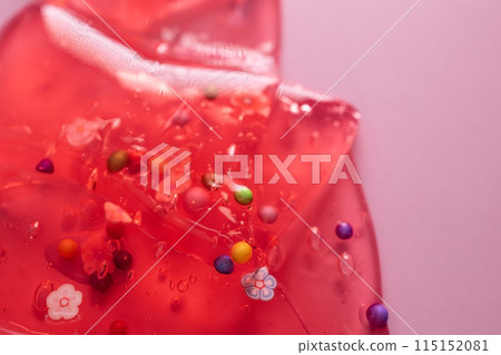 Colorful candy on a red background with water drops and bubbles. Colorful gel texture, clear skincare cream with bubbles and decorative figurines background, transparent beauty serum, colored cosmetic Colorful candy on a red background with water drops and bubbles. Colorful gel texture, clear skincare cream with bubbles and decorative figurines background, transparent beauty serum, colored cosmetic 115152081