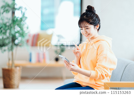 A young woman who operates a smartphone in the living room. 115153263