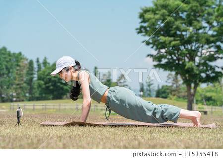 一位女士在公園裡使用瑜伽墊做瑜伽、伸展運動和鍛煉(斜坡式、俯臥撑) 一位女士在公園裡使用瑜伽墊做瑜伽、伸展運動和鍛煉(斜坡式、俯臥撑) 115155418