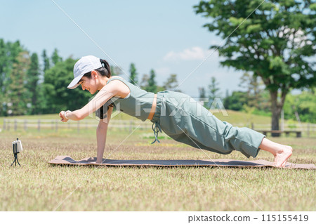 A woman who does yoga and muscle training using a smartphone app and smart watch in the park (yoga mat) 115155419